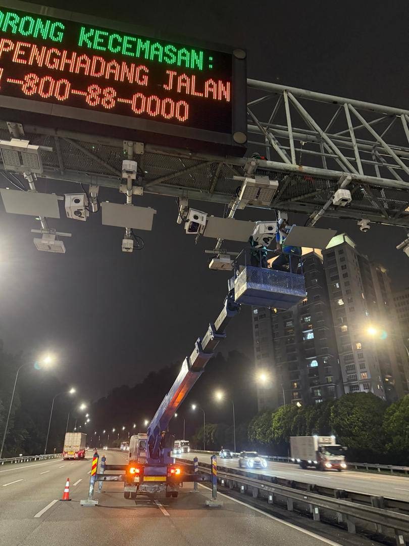 Elevated work platform servicing surveillance cameras on a highway gantry at night