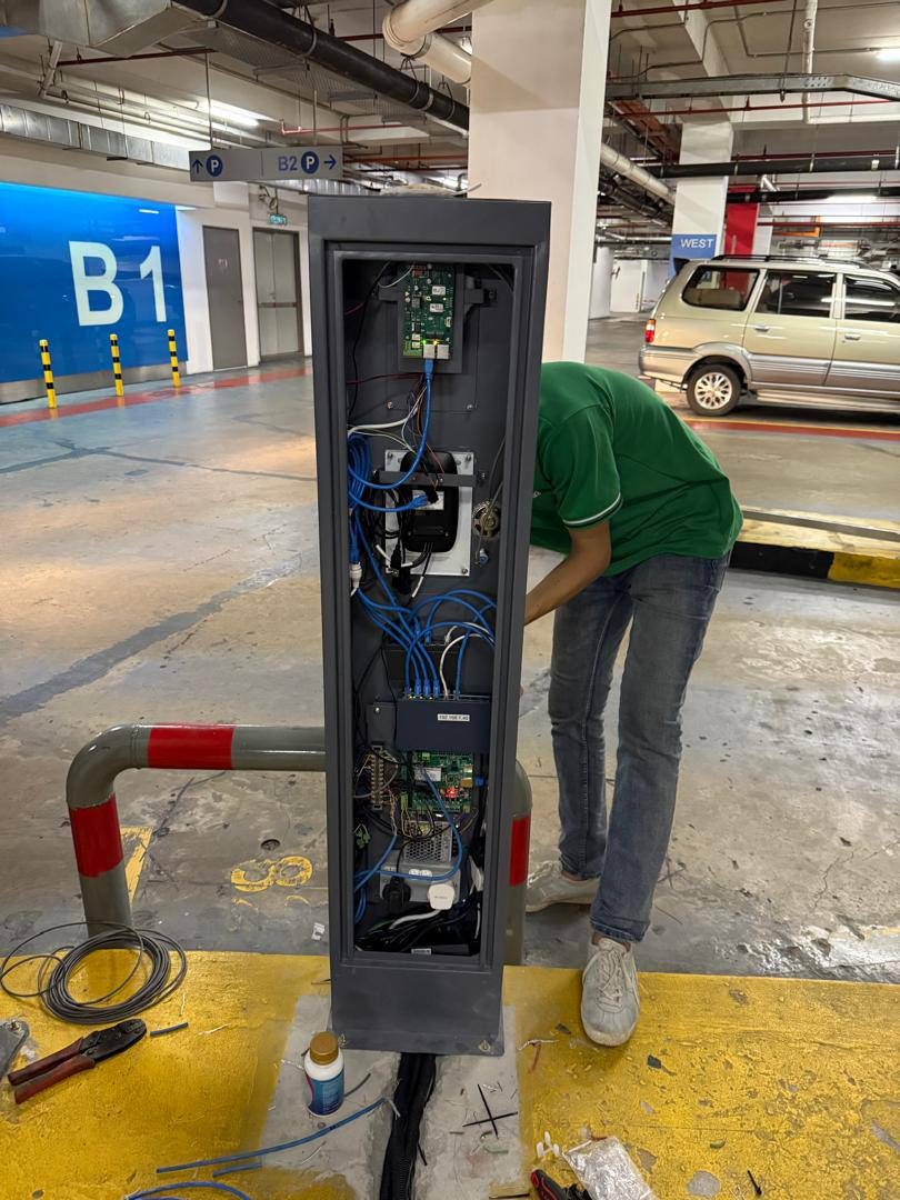 Technician wiring an automated carpark barrier control cabinet in a mall basement