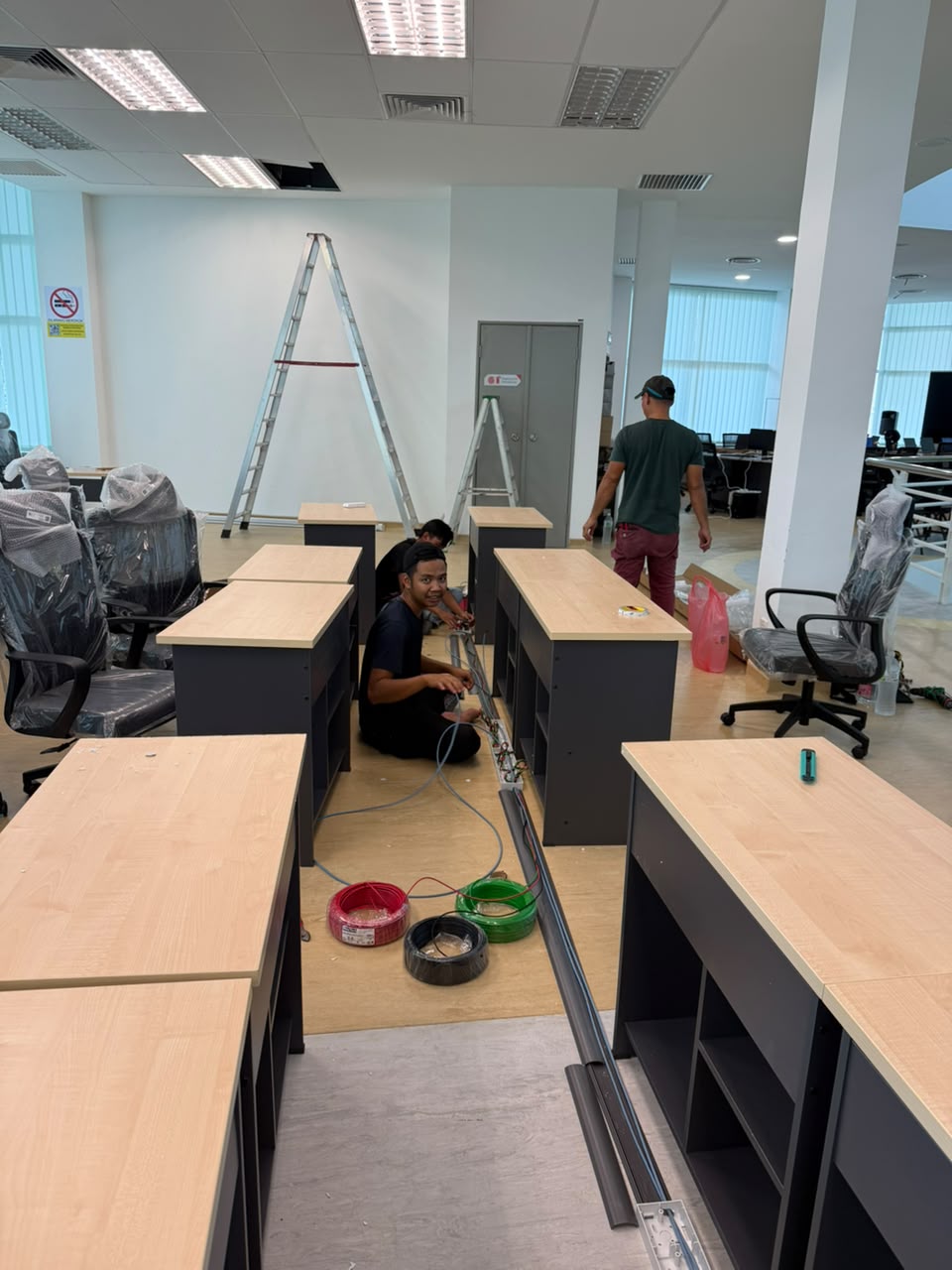 Technicians wiring structured cabling beneath rows of new office workstations during a fit-out
